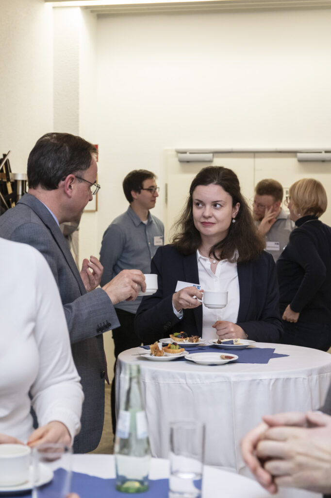Eventfotografie in Bonn. Eine Frau und ein Mann im Businessoutfit stehen an einem Stehtisch und unterhalten sich. Beide halten eine weiße Tasse in der Hand.